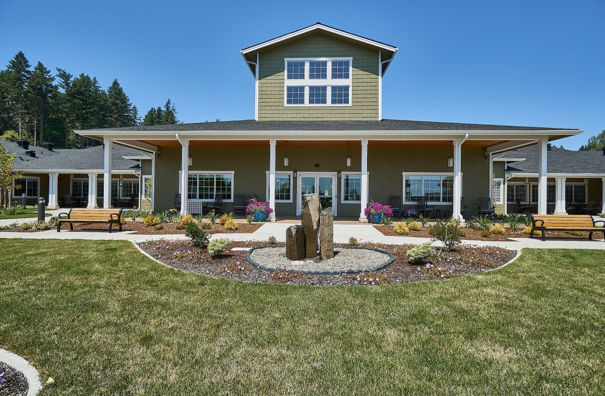 A large house with a well-maintained lawn and vibrant landscaping under a clear blue sky.