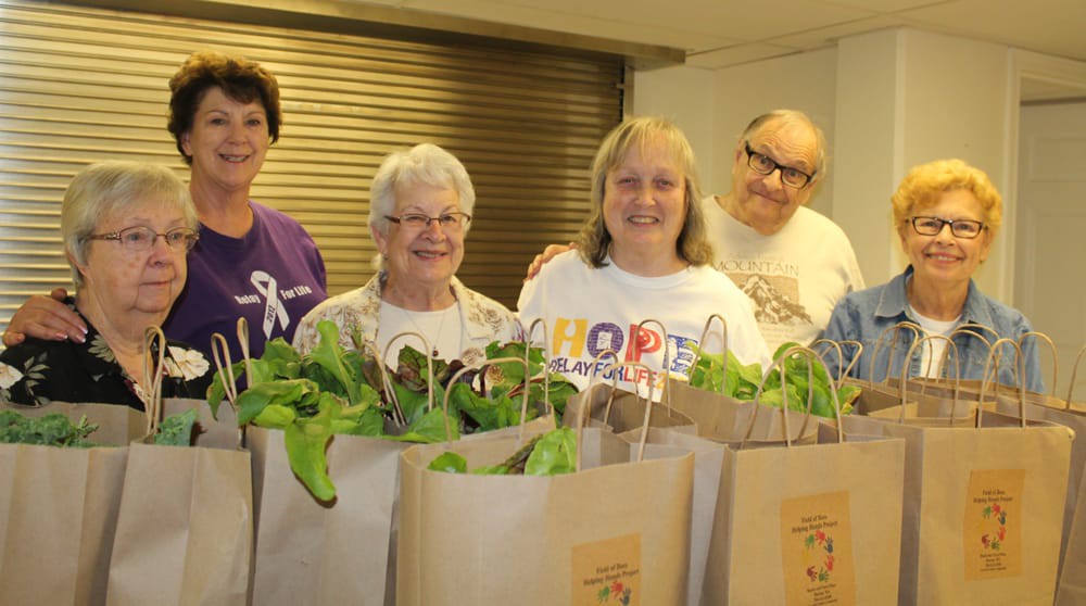 A group of volunteers standing behind bags filled with plants, participating in a community donation event.