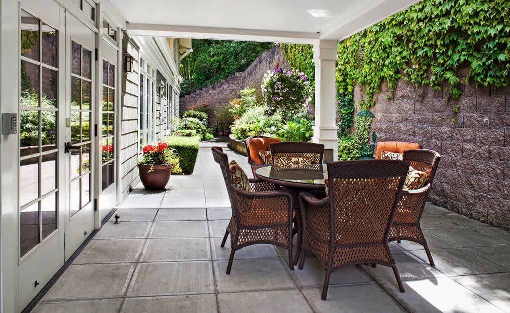 A cozy patio with a dining table and wicker chairs surrounded by lush greenery.