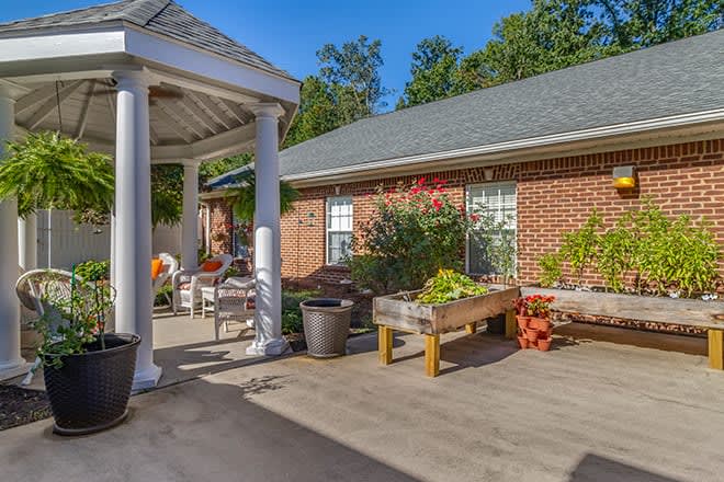 A sunny outdoor patio with garden furniture and plants, adjacent to a brick building.