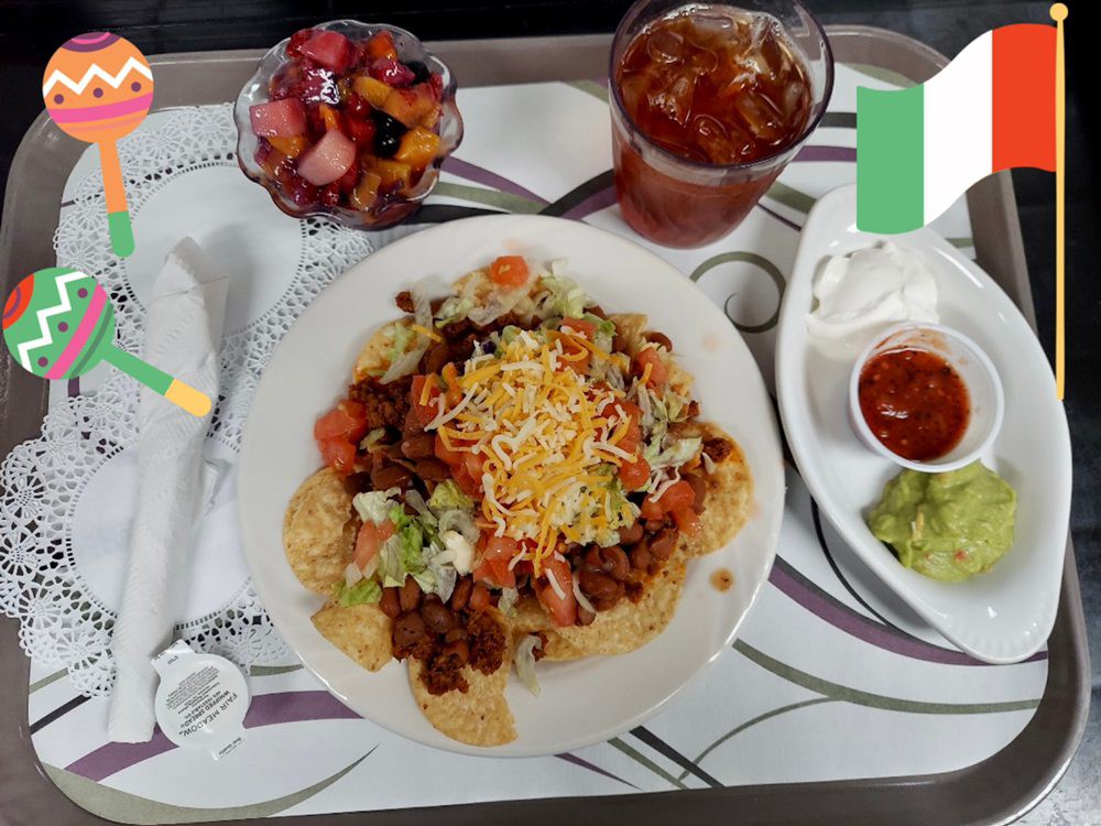A delicious Mexican meal featuring nachos with cheese, tacos, guacamole, salsa, iced tea, and a side of fruit salad.