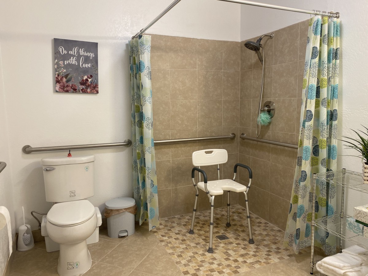 An accessible bathroom with a shower chair, grab bars, and a tiled floor for safety.