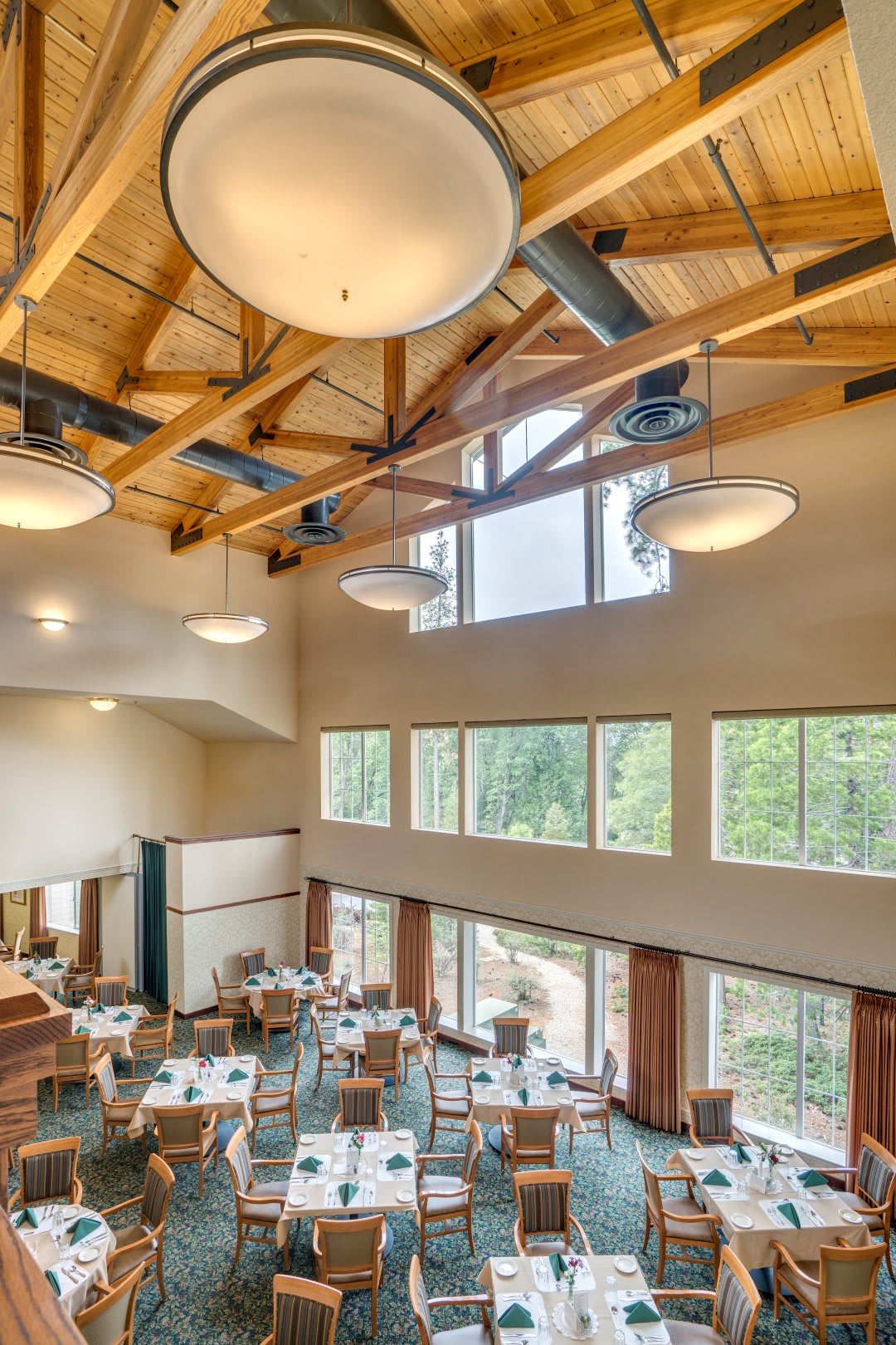 A spacious restaurant interior with wooden beams and large windows allowing natural light to illuminate the dining area.