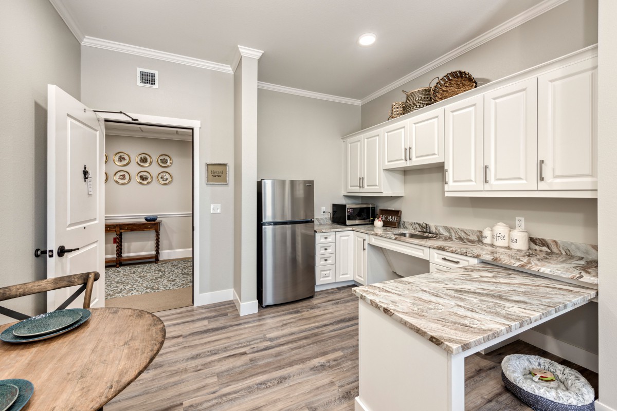 A modern kitchen with white cabinets, a stainless steel fridge, and hardwood flooring.