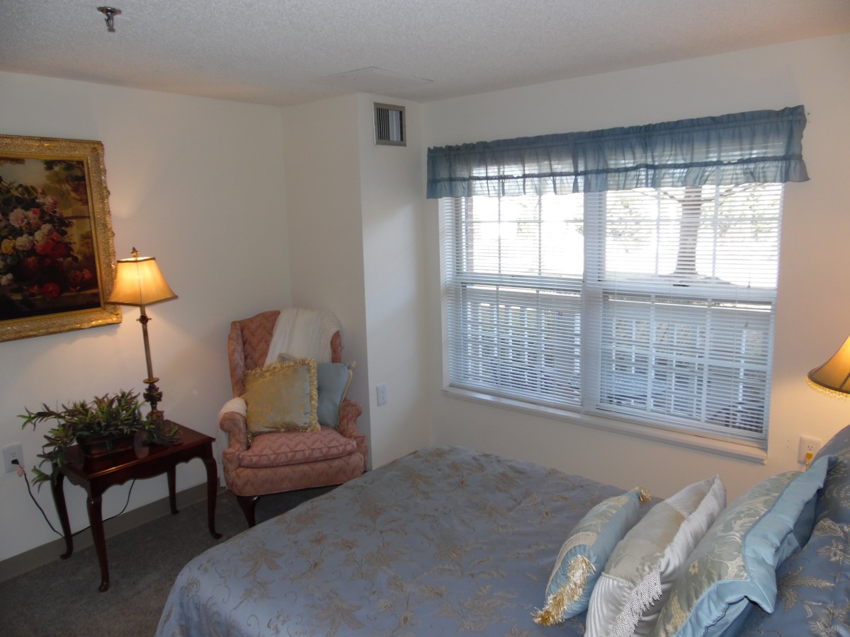 A cozy bedroom with a bed, chair, and lamp next to a window.