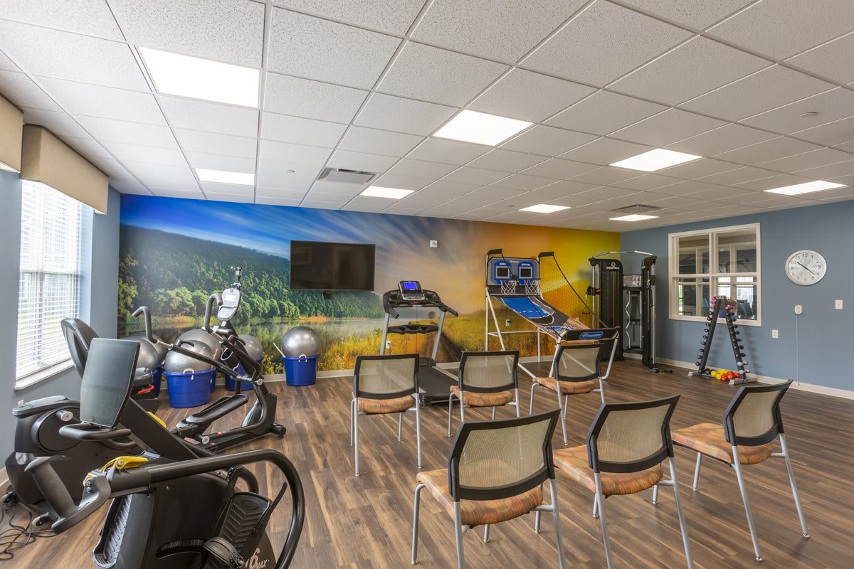 A gym with exercise equipment, chairs, a television, and a colorful mural on the wall.