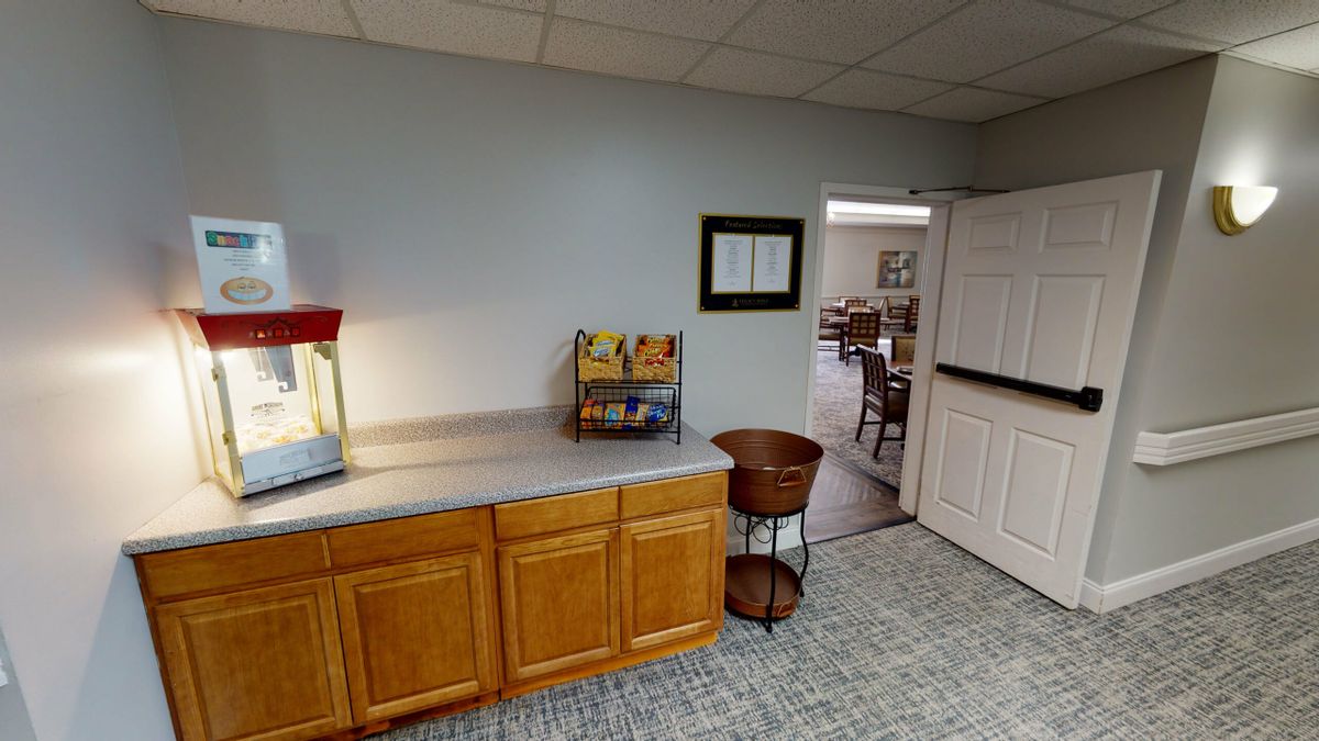 A room with a popcorn machine on a wooden cabinet, leading into another area through an open doorway.