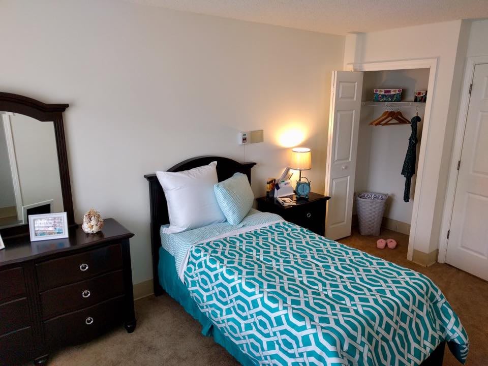 A cozy bedroom with a neatly made bed, a bedside lamp, and an open closet.
