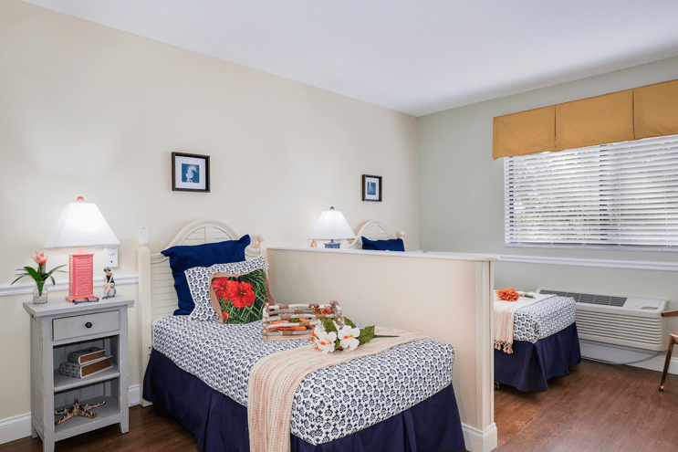 A cozy bedroom with twin beds, decorated with blue and white bedding, featuring a small table with flowers.