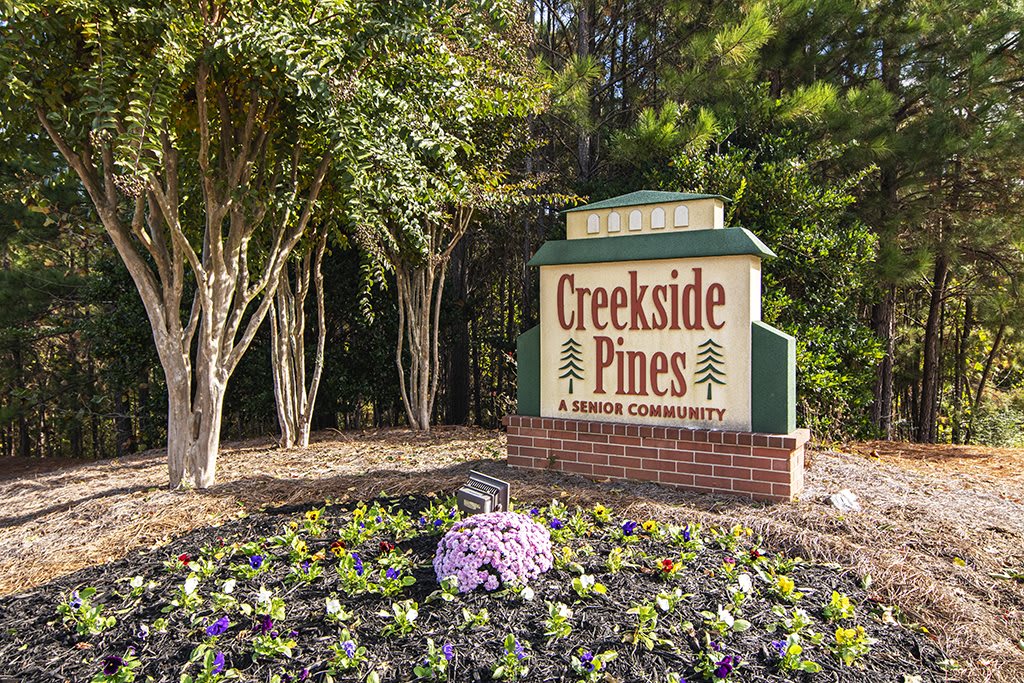 Creekside Pines community entrance sign surrounded by flowers and trees.