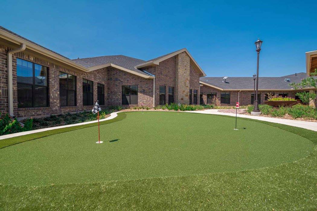 A modern building with a well-maintained putting green in the foreground under a clear blue sky.