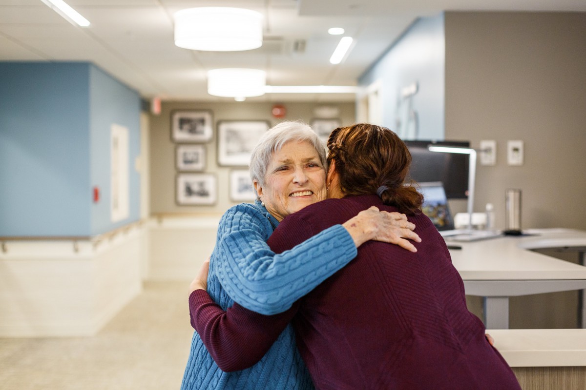 An elderly woman receiving a warm hug in a healthcare setting.