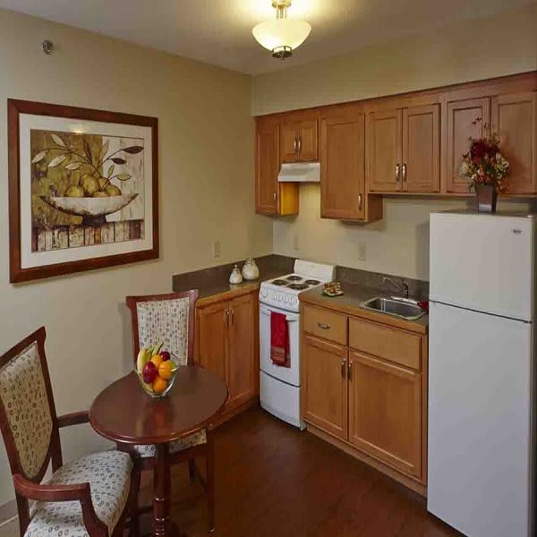 A small kitchenette with a dining table and chairs, featuring wood cabinets, a refrigerator, and a stove.