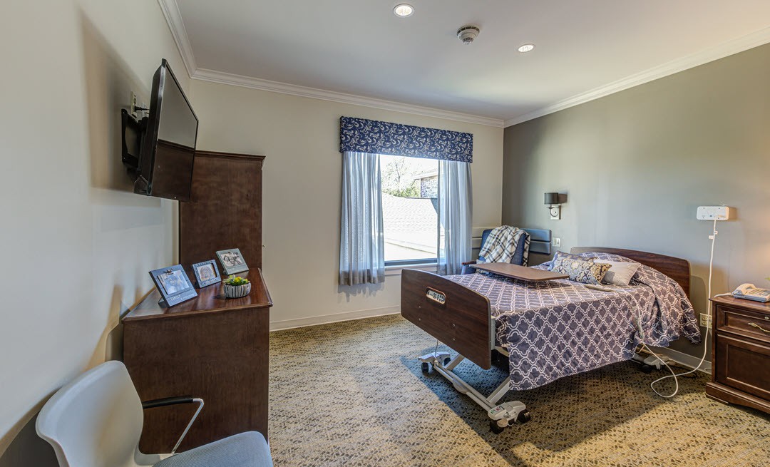 A well-furnished hospital room with a bed, television, and large window for natural light.