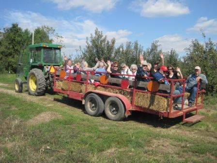 A group of people enjoying a hayride on a farm under a sunny sky.