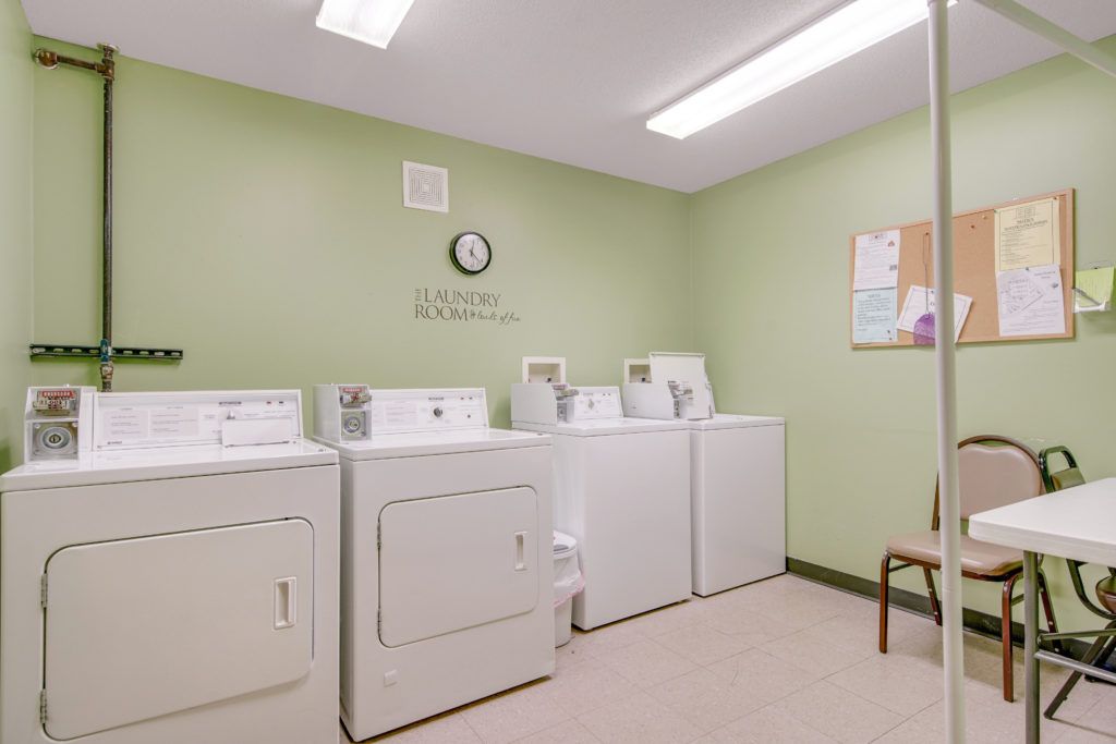 A tidy laundry room with washers and dryers lined up against a green wall.