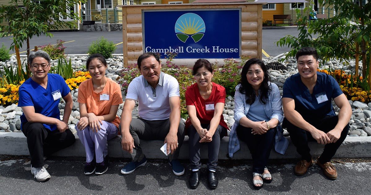 A group of people sitting in front of the Campbell Creek House sign.