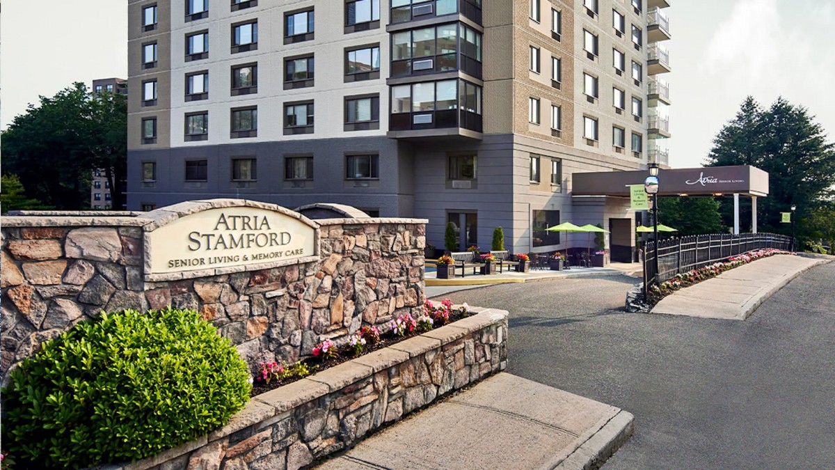 The entrance to Atria Stamford, featuring well-maintained landscaping and a welcoming sign.