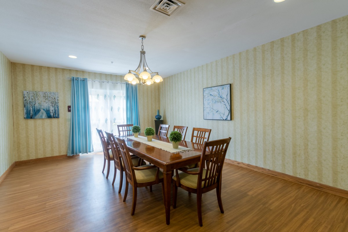 A spacious dining room with a large table and chairs, complemented by a chandelier and bright curtains.