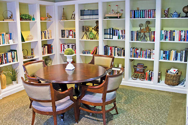 A cozy reading area featuring a round table, surrounded by bookshelves filled with books and decorative items.