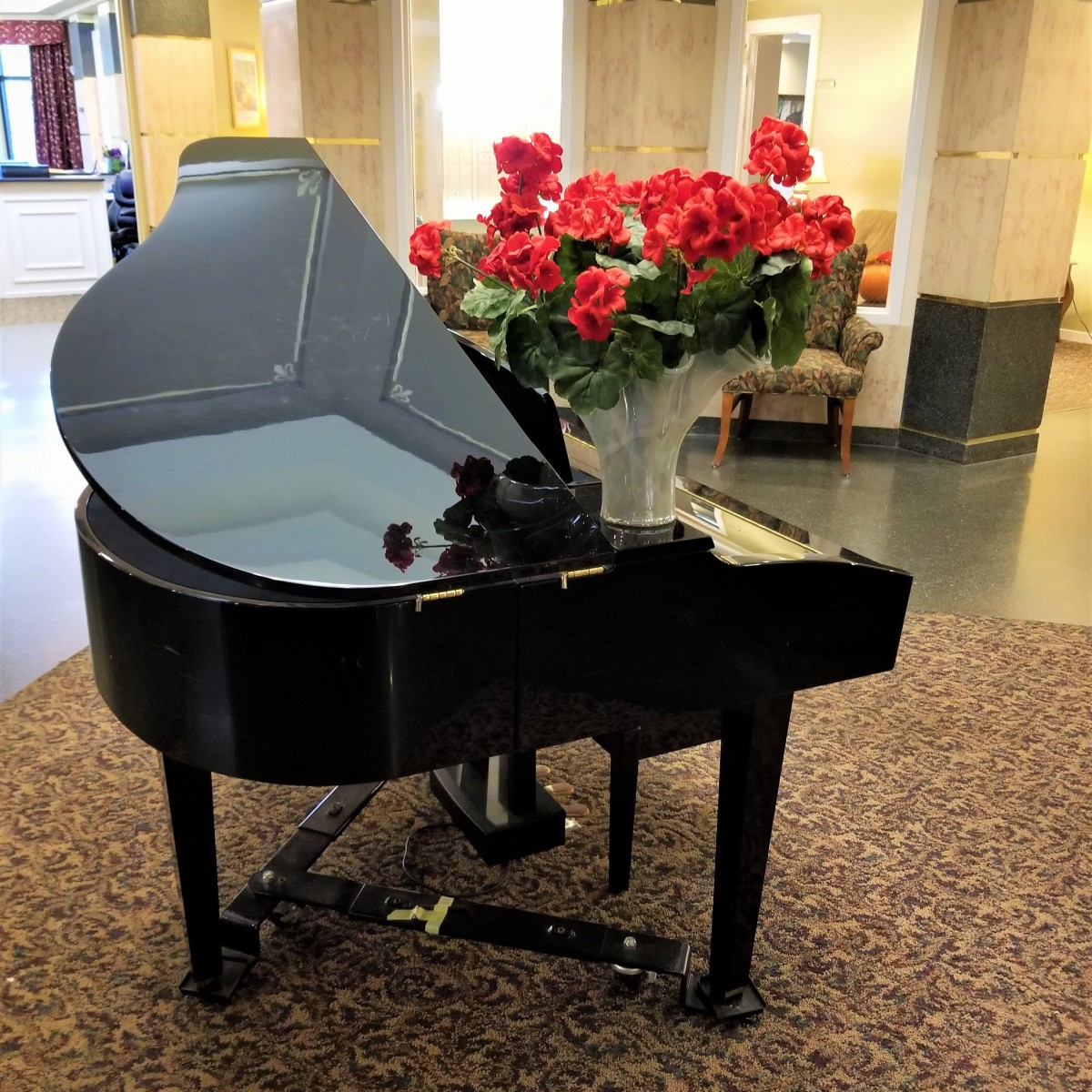 A black grand piano adorned with a bouquet of red roses in a lobby setting.