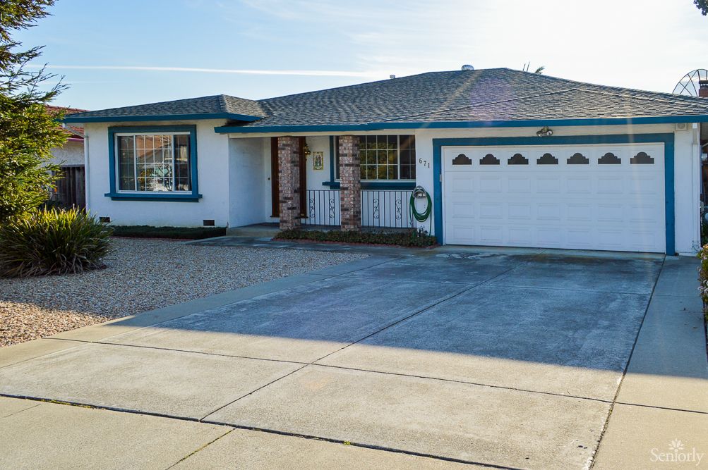 A single-story house with a blue trim, featuring a two-car garage and a spacious driveway.
