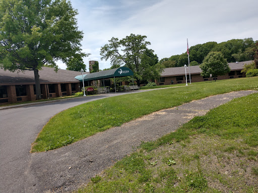 A view of a well-kept building surrounded by lush green grass and trees, featuring a flagpole and a paved pathway.