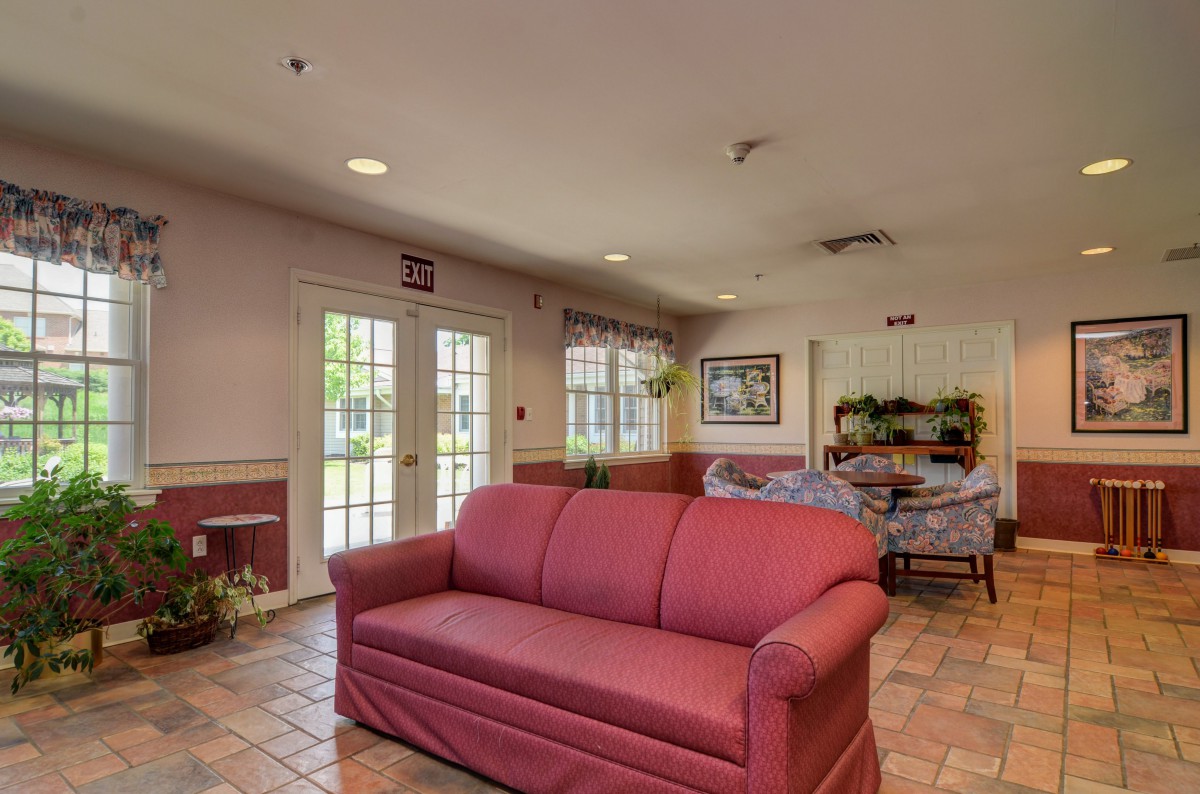A cozy living room featuring a red sofa, artwork on the wall, and natural light streaming through the windows.