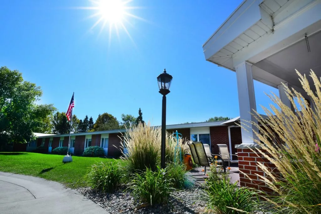 A sunny day outside a building with an American flag and surrounding greenery.