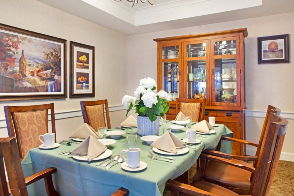 A well-decorated dining room with a table elegantly set for a meal, featuring a green tablecloth and a centerpiece of white flowers.