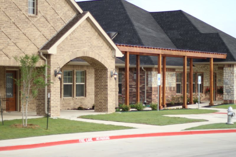 A suburban brick house with a well-manicured lawn and a shaded porch area.