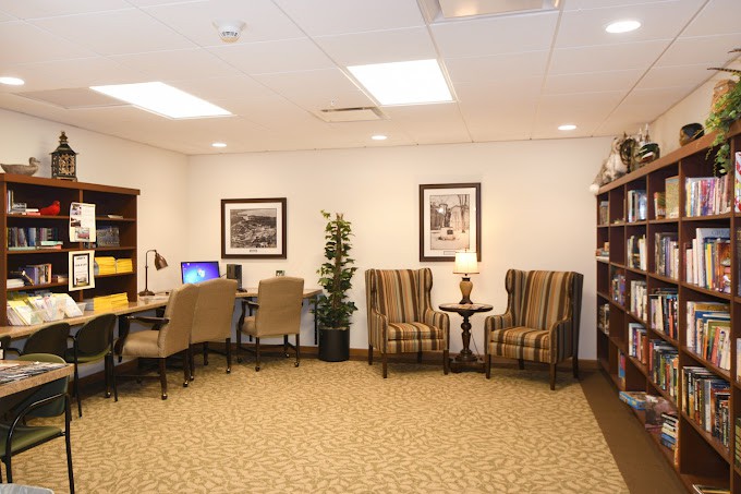 A cozy office lounge area featuring desks with computers, comfortable chairs, a bookshelf, and decorative artwork on the walls.
