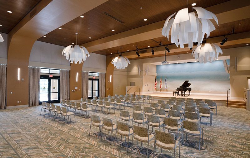 A modern auditorium with a grand piano on stage and rows of empty chairs.