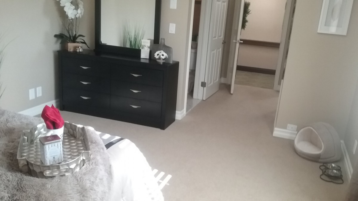 A cozy bedroom featuring a dresser with a mirror, light carpet, and neutral decor.