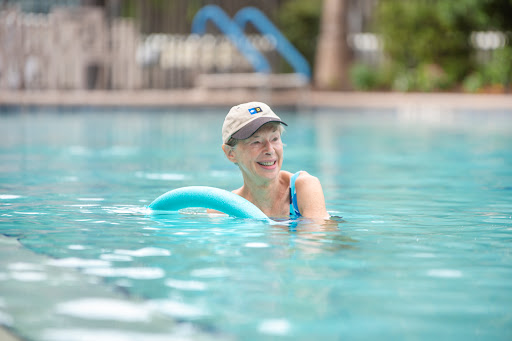 A person enjoys a relaxing day at the pool, using a foam noodle for support while swimming.