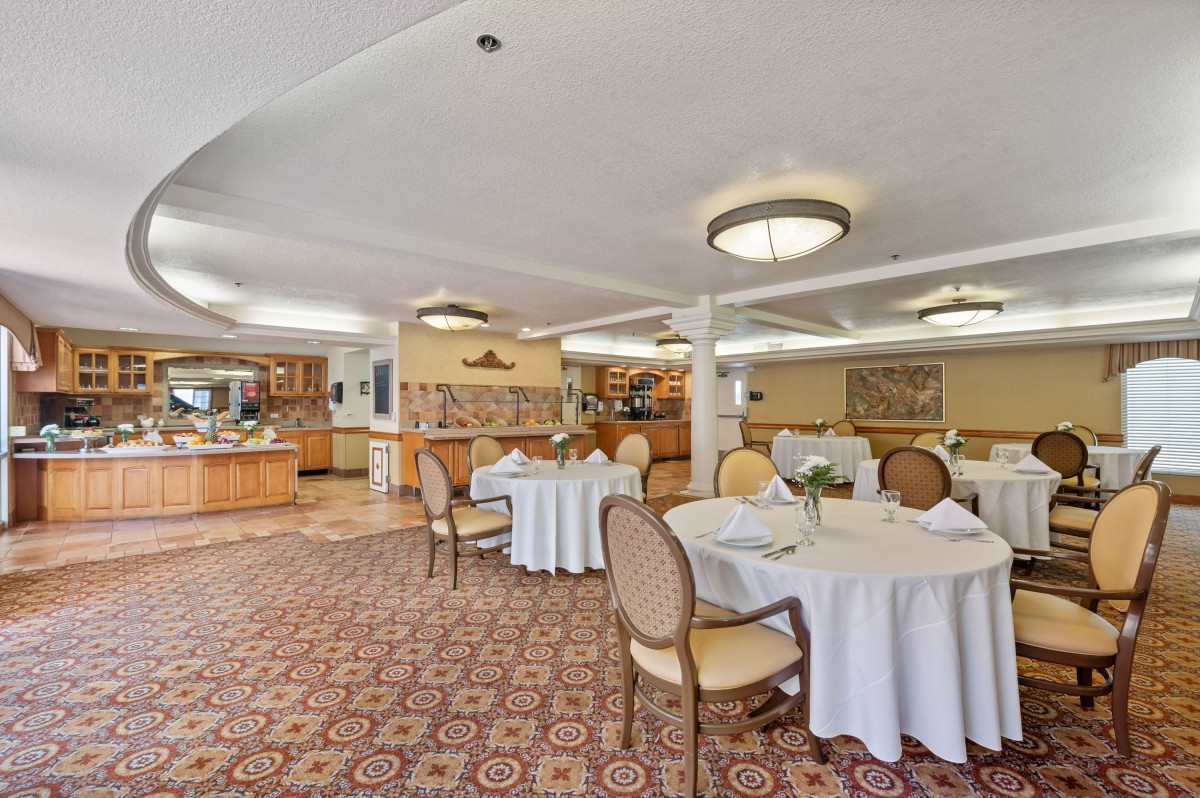 An elegant dining room with round tables and upholstered chairs, featuring a carpeted floor and chandeliers.