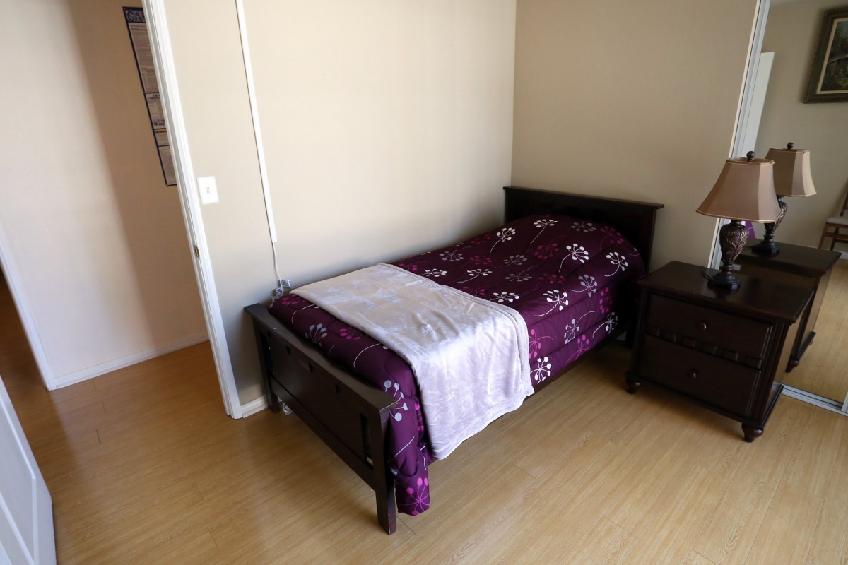A minimalist bedroom featuring a single bed with purple bedding and a nightstand.