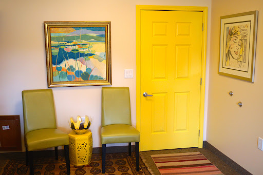A vibrant interior space featuring a yellow door, green chairs, and a colorful piece of art.