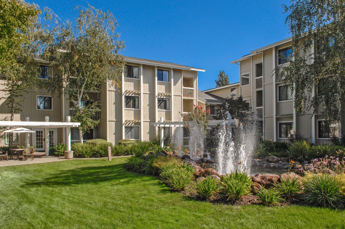 A view of a residential apartment complex with a fountain and landscaped gardens.
