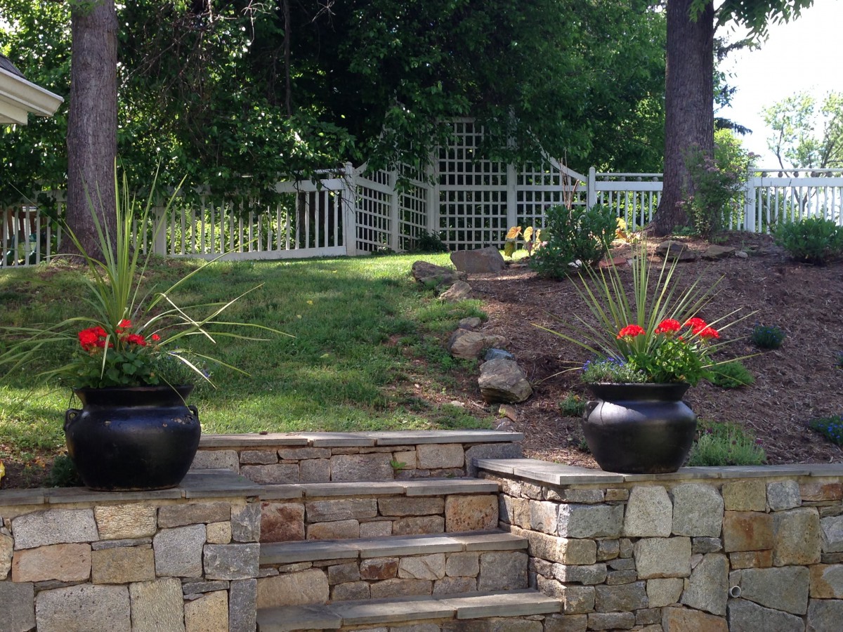A serene garden with stone steps leading up to a white fence, flanked by planters.