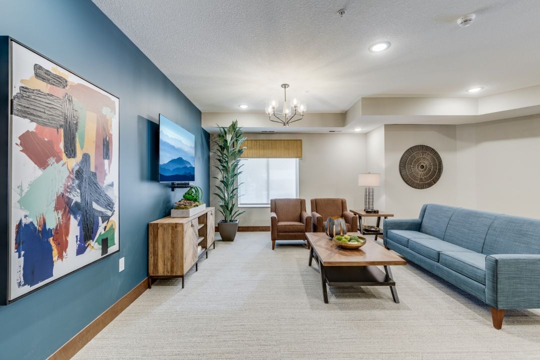 A modern living room with stylish furniture and decor, featuring a blue accent wall, comfortable seating, and a flat-screen TV.