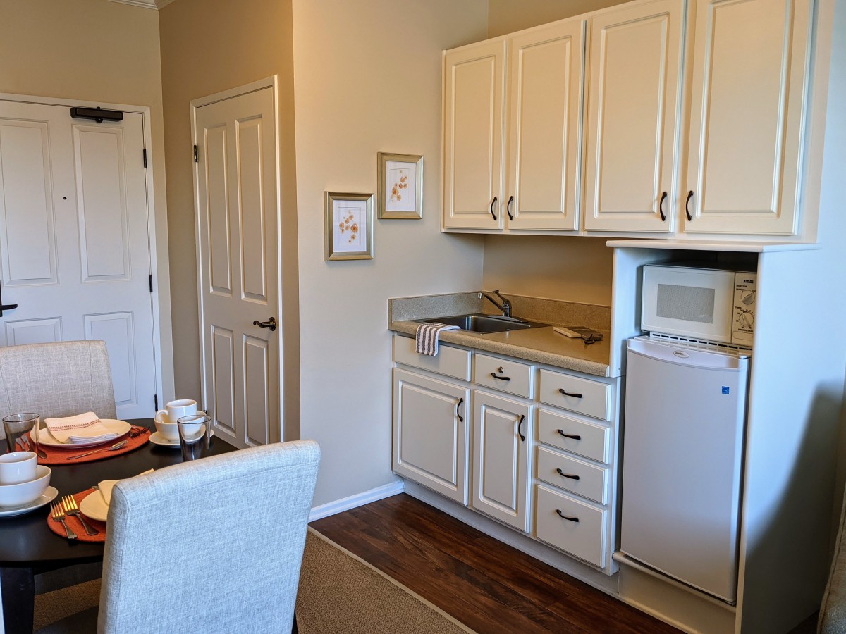 Compact kitchen space with white cabinets, a mini fridge, and microwave adjacent to a small dining area.