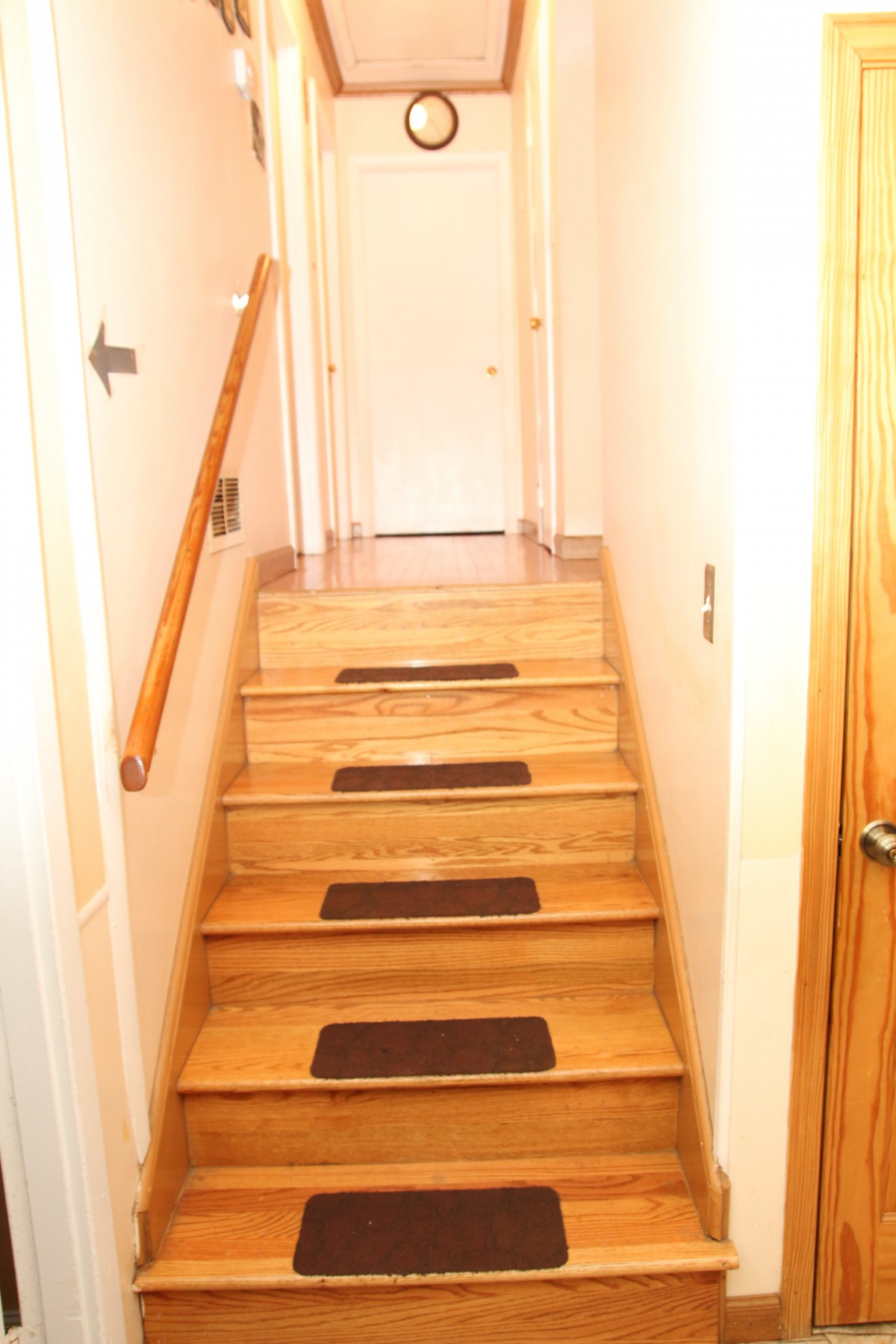 A wooden staircase with safety strips and a handrail in a well-lit hallway.