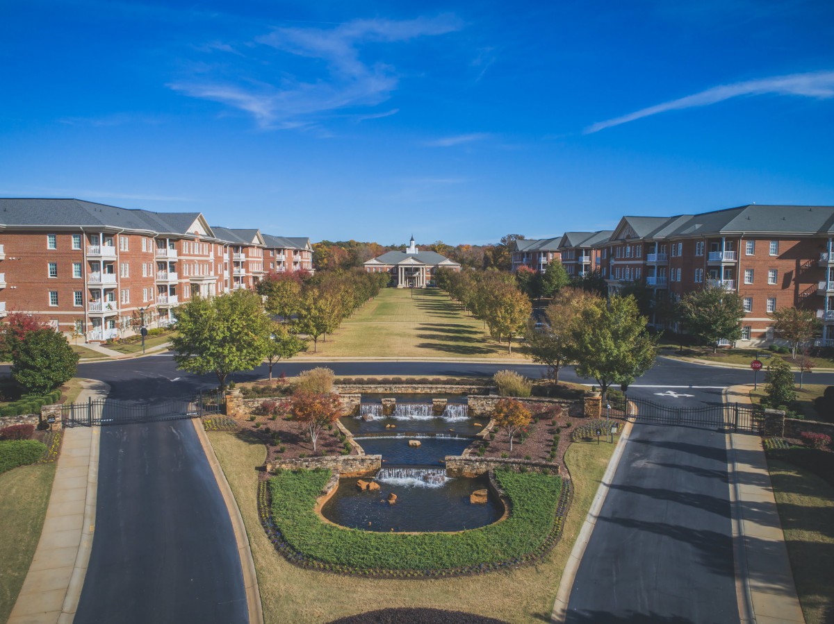 Aerial view of a landscaped residential complex with buildings, roads, and a central fountain.