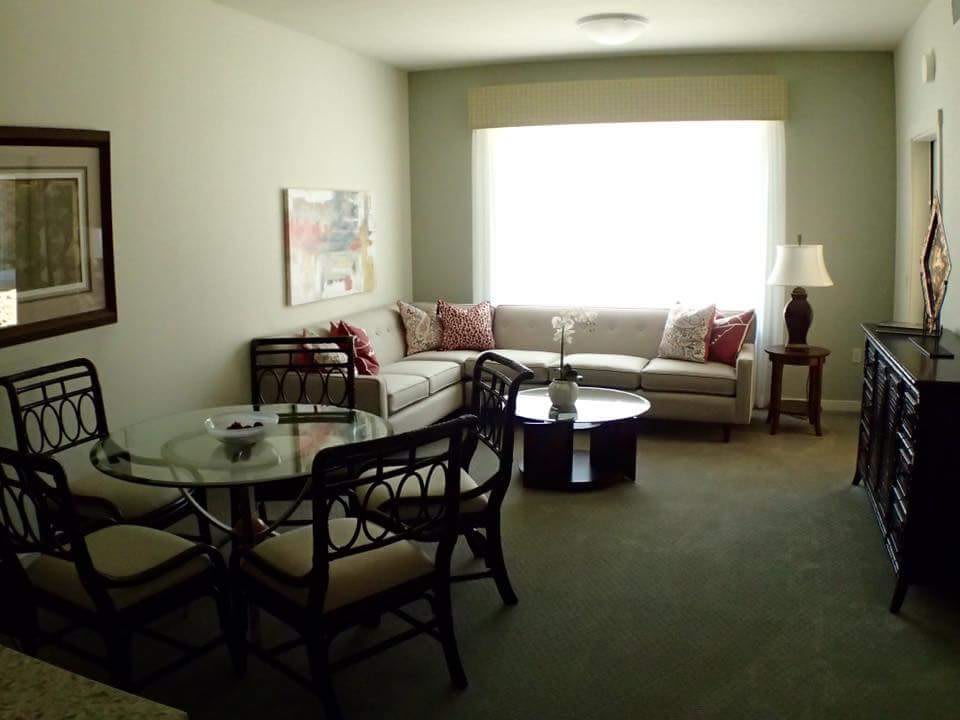 A cozy living room with a sofa, round table, chairs, and a large window.