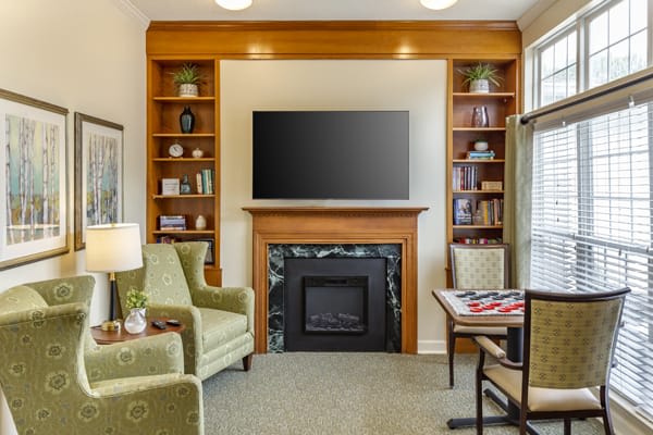 A cozy living room with a fireplace, television, and bookshelves surrounded by comfortable armchairs.