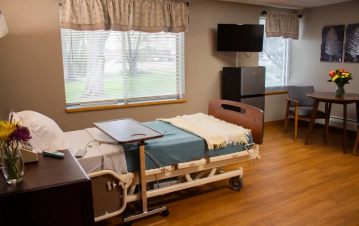 A hospital room featuring a bed, tray table, and television, with natural light coming through the windows.