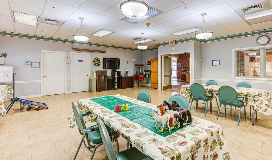 A community room with tables and chairs arranged for activities, featuring ceiling lights and decorative items.