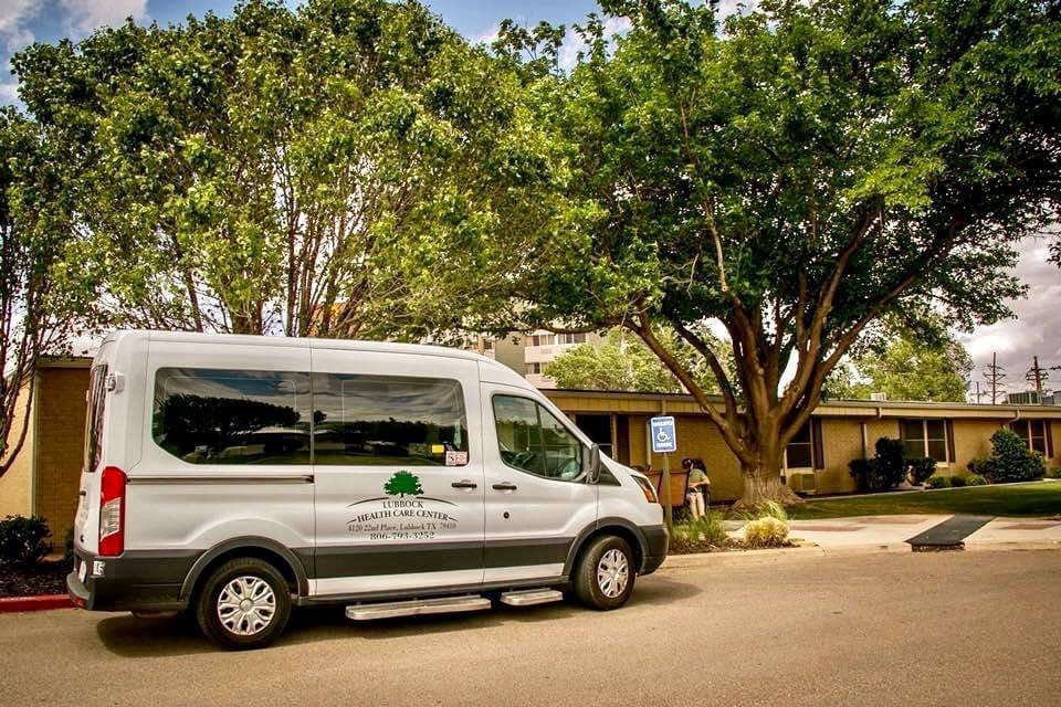A white van parked under a large tree near a building.