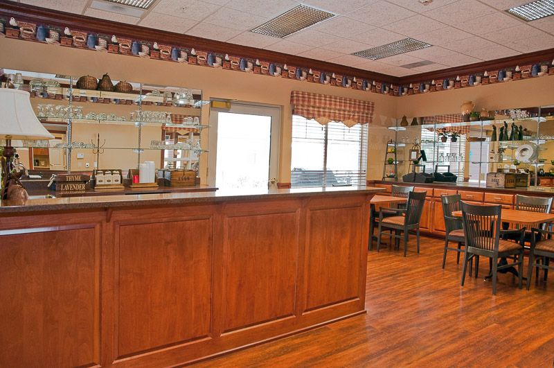 An empty bar area with a wooden counter, chairs, and shelves within a well-lit interior space.